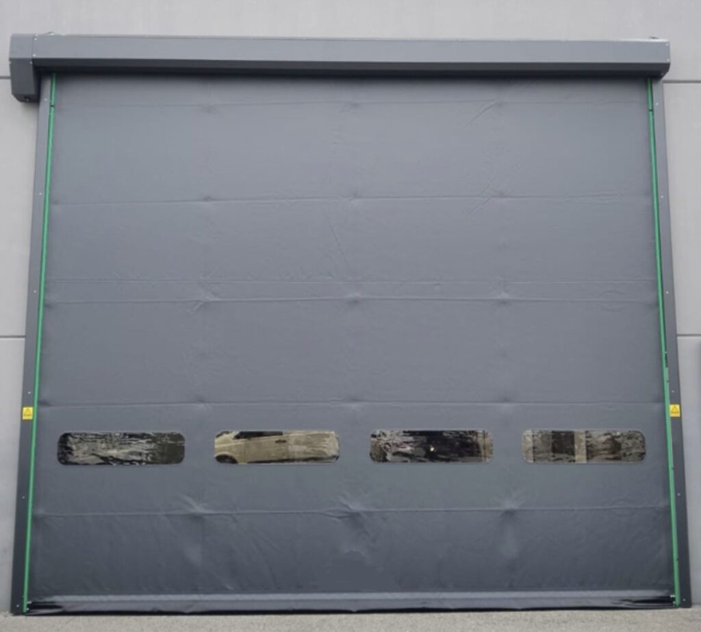 Porta rapida industriale grigio scuro con una banda di finestrature e cassonetto in alto, installata all'esterno di un edificio in provincia di Vicenza