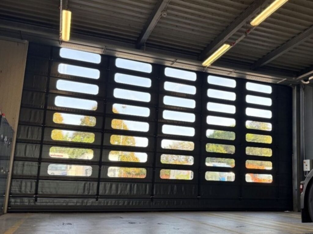 Porta rapida industriale grigio scuro con file di finestrature trasparenti, vista dall'interno di un capannone in provincia di Vicenza con una motrice di camion parcheggiata