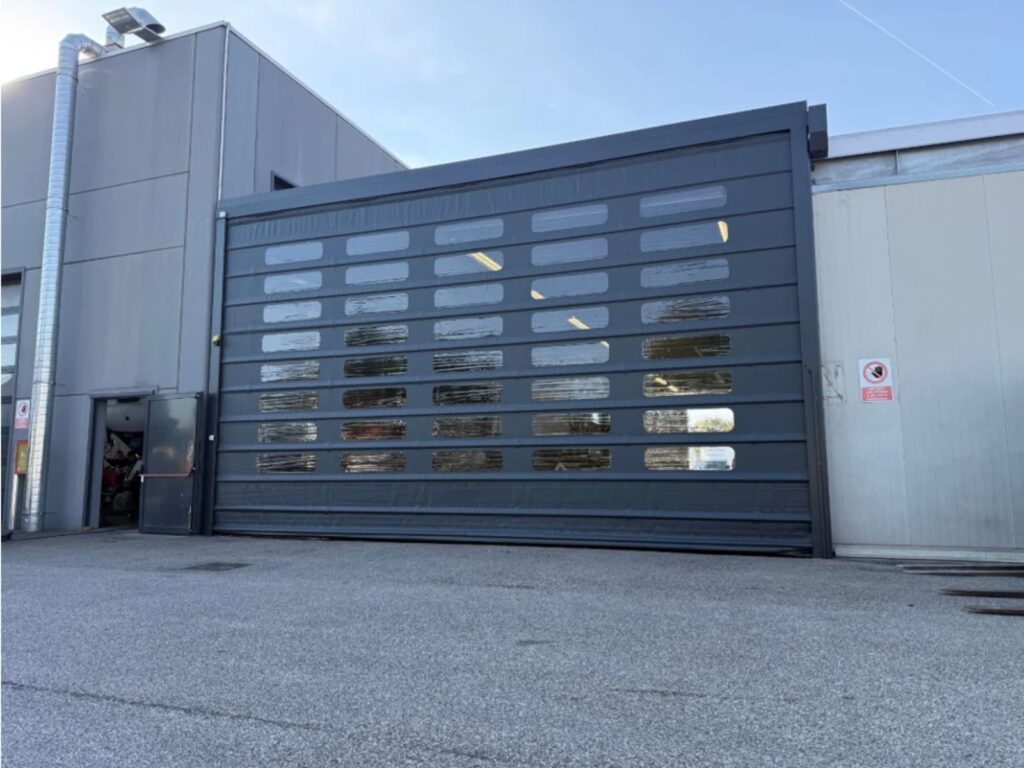 Porta rapida industriale grigio scuro di grandi dimensioni con file di finestrature, installata sulla facciata esterna di un capannone in provincia di Vicenza